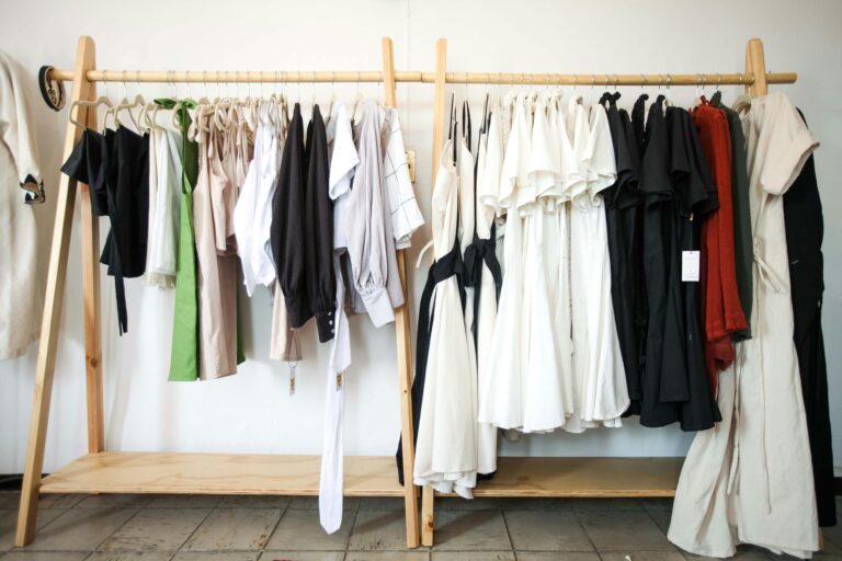A variety of stylish clothes hanging on a wooden clothing rack indoors.